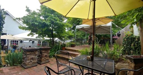 A cozy outdoor patio with yellow umbrellas, stone planters, and lush greenery, perfect for dining or relaxing.
