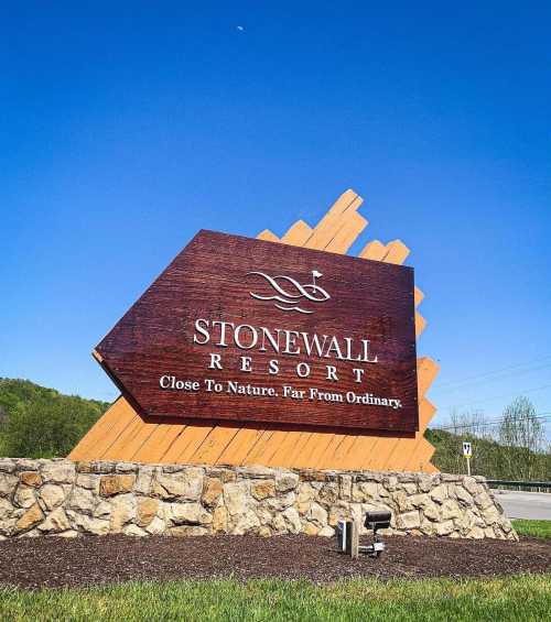 Sign for Stonewall Resort, featuring a wooden design with the slogan "Close To Nature, Far From Ordinary" against a clear blue sky.