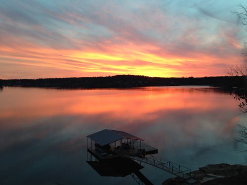 A serene lake at sunset, reflecting vibrant colors in the sky and water, with a small dock in the foreground.