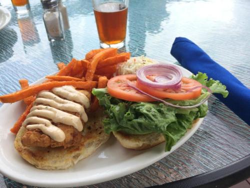 A plate with a fried chicken sandwich topped with lettuce, tomato, and onion, served with sweet potato fries and a drink.