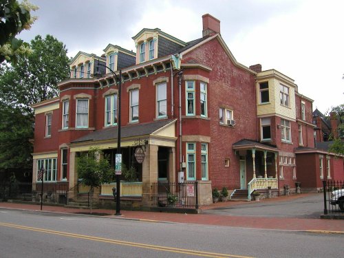 Historic red brick building with multiple stories, decorative trim, and a welcoming porch, set along a tree-lined street.