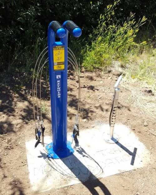 A blue bike repair station with tools and a pump, set in a grassy area.