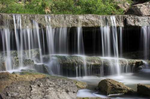 A serene waterfall cascading over rocky ledges, surrounded by lush greenery and smooth stones.