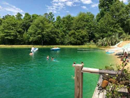 A serene green pond surrounded by trees, with people swimming and relaxing on inflatable rafts.