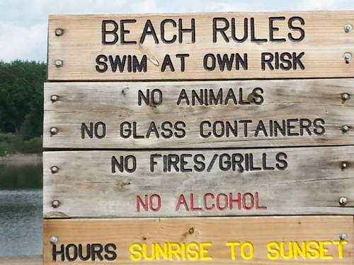 Wooden sign listing beach rules: swim at own risk, no animals, no glass, no fires/grills, no alcohol, hours sunrise to sunset.