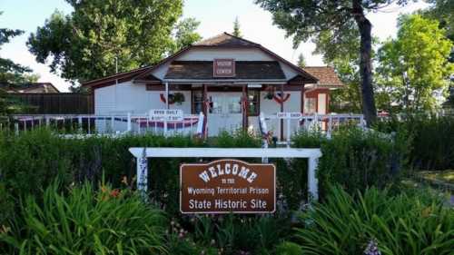 A historic building with a sign reading "Welcome to the Wyoming Territorial Prison State Historic Site," surrounded by greenery.