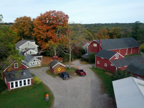 Aerial view of a rural farm with red barns, houses, and autumn trees in vibrant colors.