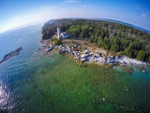Aerial view of a coastal landscape featuring a lighthouse, rocky shore, and lush greenery along the water's edge.