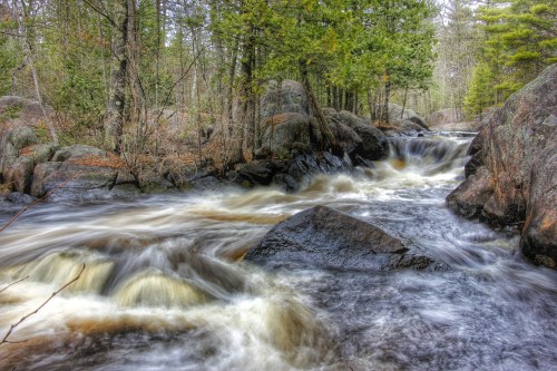 A flowing river cascades over rocks, surrounded by lush green trees and a serene natural landscape.