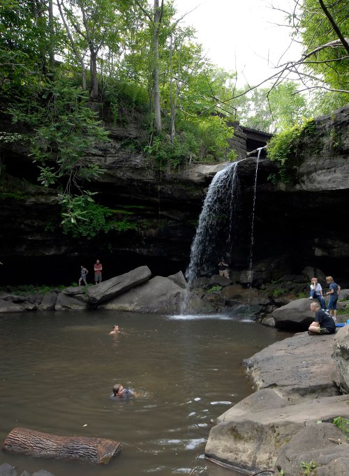 A serene waterfall cascades into a rocky pool, with people swimming and enjoying the natural surroundings.