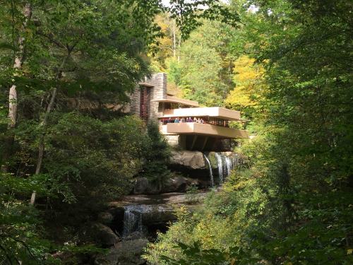 A modern house nestled in a lush forest, overlooking a waterfall and surrounded by vibrant autumn foliage.