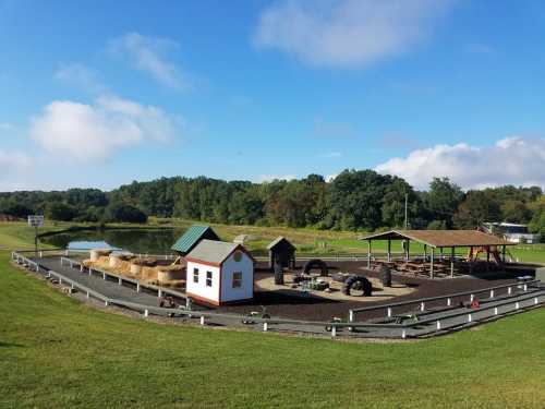 A scenic view of a farm area with a pond, hay bales, and play structures under a clear blue sky.