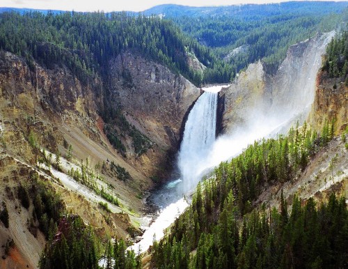 A stunning waterfall cascades down a rocky cliff, surrounded by lush green forests and rugged terrain.