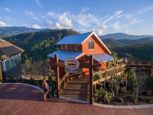 A scenic view of a wooden cabin surrounded by mountains and greenery, with a pathway leading to the entrance.