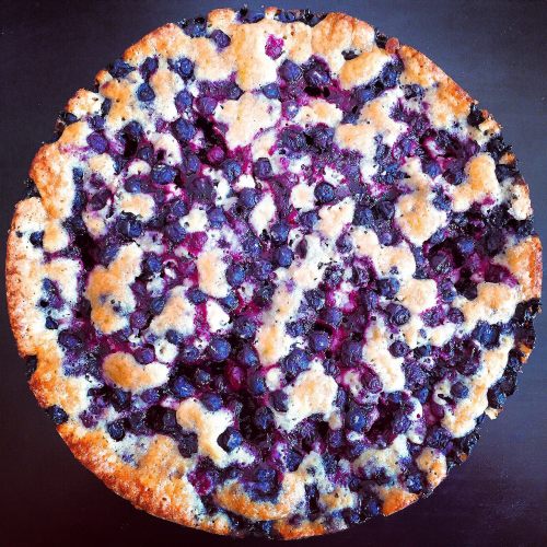 A round blueberry pie with a golden crust and a filling of dark blue and purple berries.