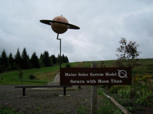 A large model of Saturn with its moon Titan, set in a grassy area with a sign identifying the display.