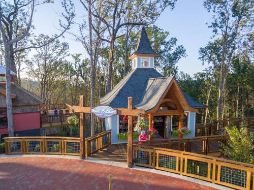 A charming wooden gazebo surrounded by trees, featuring a peaked roof and colorful flower arrangements.