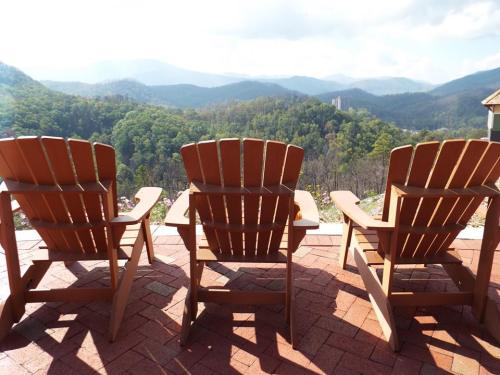 Three wooden chairs facing a scenic mountain view with lush greenery and a cloudy sky in the background.