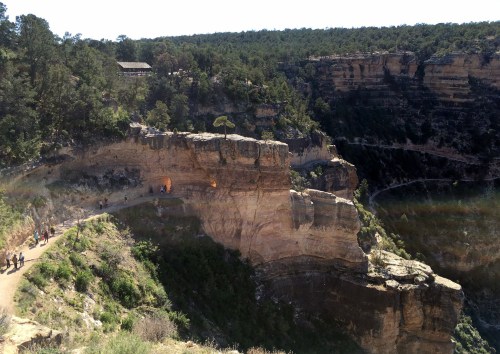 A scenic view of a canyon with a winding path and visitors, surrounded by lush greenery and rocky cliffs.