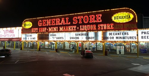 Brightly lit general store with signs for gifts, liquor, snacks, and more, set in a nighttime scene.