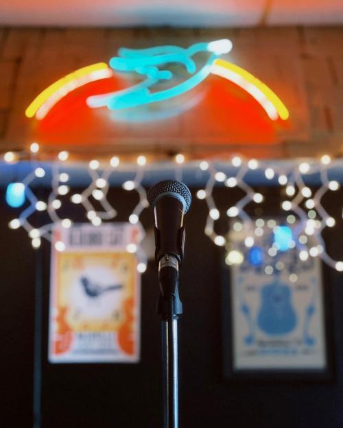 A microphone in front of colorful neon lights and string lights, with music posters in the background.