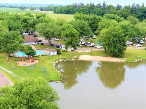 Aerial view of a campground with a pool, playground, and a serene lake surrounded by lush greenery.