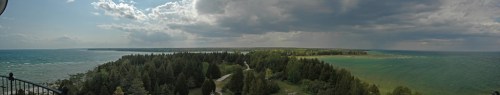 A panoramic view of a coastline with lush green trees and a blue lake under a partly cloudy sky.