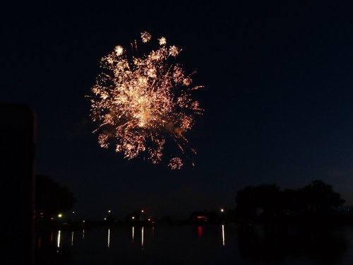 Colorful fireworks burst in the night sky, reflecting on a calm body of water below.