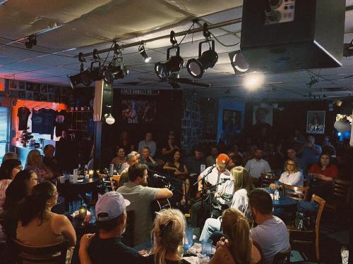 A lively music venue with a crowd enjoying a live performance on stage, illuminated by soft lighting.