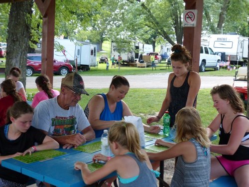 A group of people, including children and adults, gather around a blue picnic table, engaged in an activity outdoors.