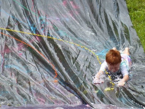 A child slides down a colorful water slide, splashing water as they enjoy a sunny day outdoors.