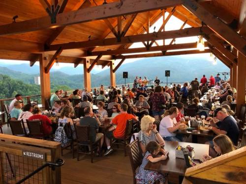 A bustling restaurant with a wooden interior, filled with diners enjoying meals and a scenic mountain view.