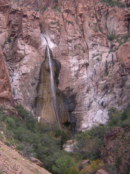 A waterfall cascading down a rocky cliff surrounded by greenery in a rugged landscape.