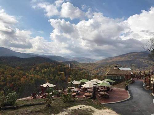 Scenic view of a mountain landscape with colorful autumn trees, outdoor seating, and a cloudy sky.