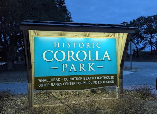 Sign for Historic Corolla Park, featuring attractions like Currituck Beach Lighthouse and Outer Banks Center for Wildlife Education.
