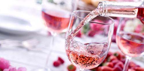 A glass being filled with pink wine, surrounded by fresh berries and flowers on a table.