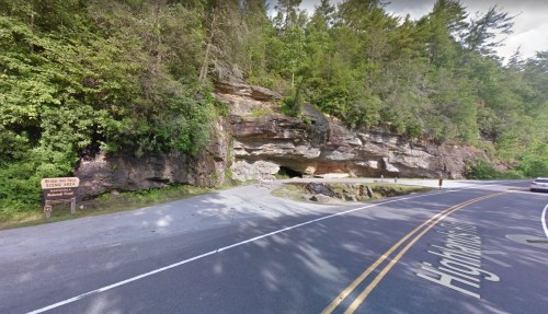 A scenic view of a rocky outcrop with trees, a road sign, and a winding road in a natural setting.
