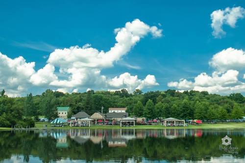 A serene lake reflects a vibrant blue sky with fluffy clouds and a charming lakeside community in the background.