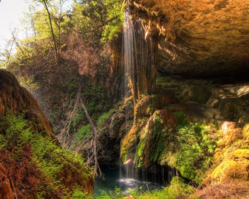 A serene waterfall cascades over moss-covered rocks into a tranquil pool, surrounded by lush greenery.