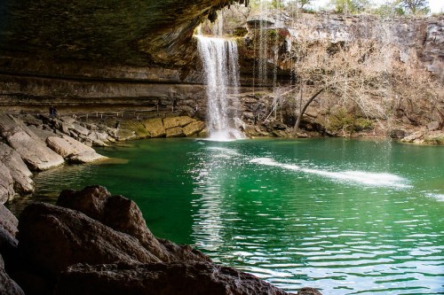 A serene waterfall cascades into a turquoise pool surrounded by rocky cliffs and bare trees.