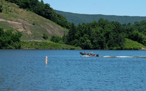 A boat speeds across a calm lake surrounded by green hills under a clear blue sky.