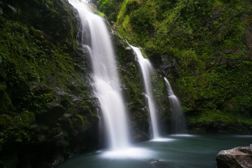 A serene waterfall cascading over moss-covered rocks into a tranquil pool, surrounded by lush greenery.