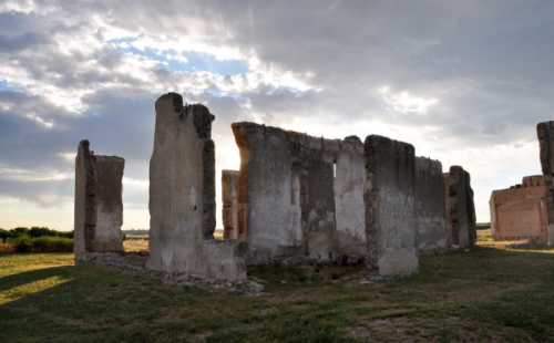 Ruins of a stone structure under a cloudy sky, surrounded by grassy fields.