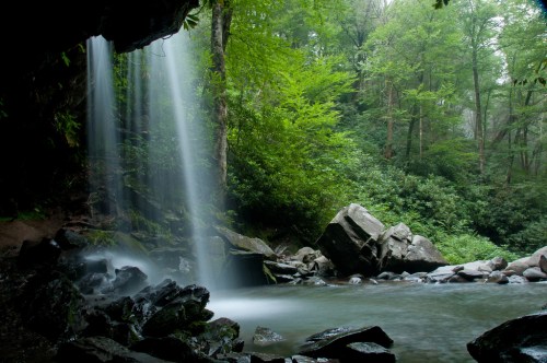 A serene waterfall cascades into a tranquil pool, surrounded by lush greenery and rocky terrain.