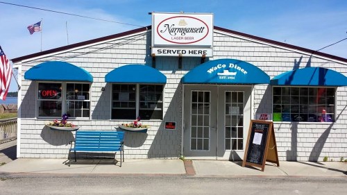A diner with blue awnings, a bench, and flower boxes, featuring an "Open" sign and a chalkboard menu outside.