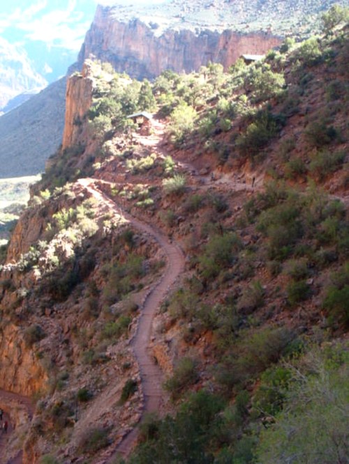 Winding trail through rocky terrain with lush greenery, set against a backdrop of steep canyon walls.