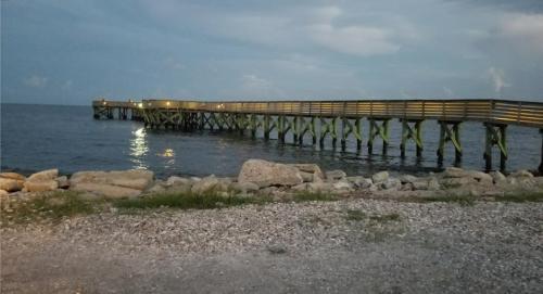 A wooden pier extends into calm waters under a cloudy sky, with lights illuminating the structure at dusk.
