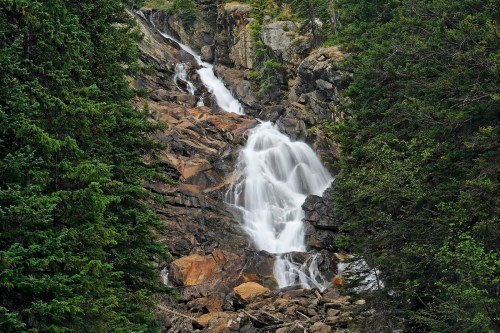A cascading waterfall flows over rocky terrain, surrounded by lush green trees.