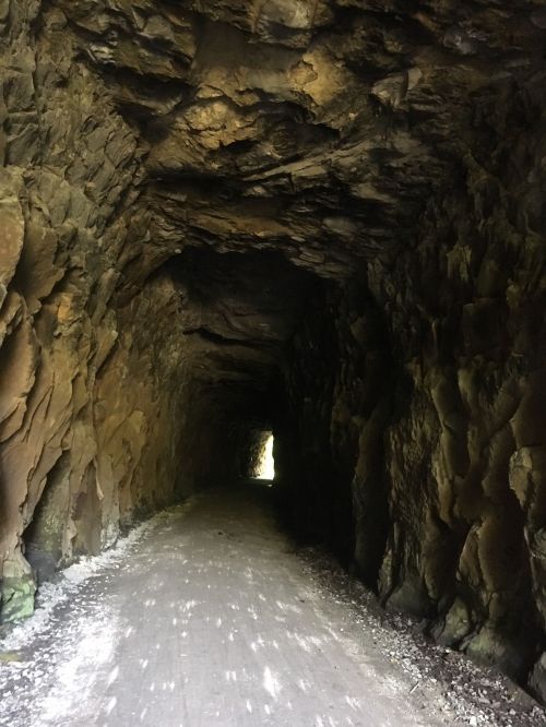 A dimly lit tunnel with rocky walls and a visible light source at the far end, leading to an open area.