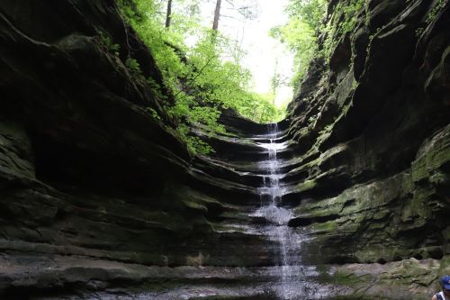 A serene waterfall cascading down moss-covered rock formations in a lush, green canyon.